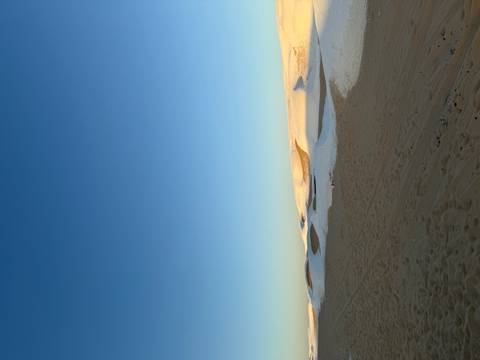 Vast desert landscape with patches of white sand under a clear blue sky.