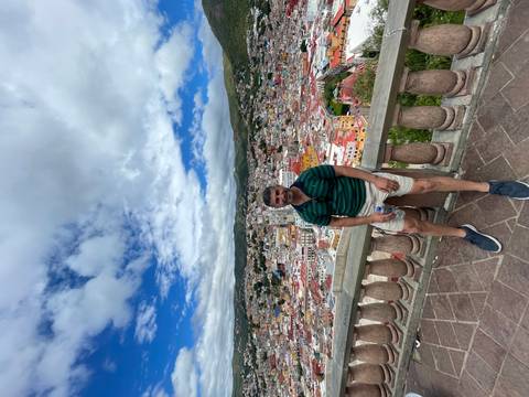       A person sitting on a balcony overlooking a colorful cityscape.
  