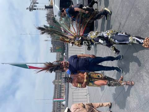 Person posing with costumed performers in a city square.