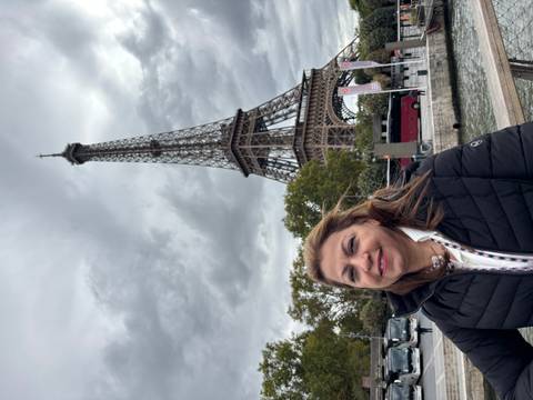 Woman smiling in front of the Eiffel Tower in Paris with clouds.