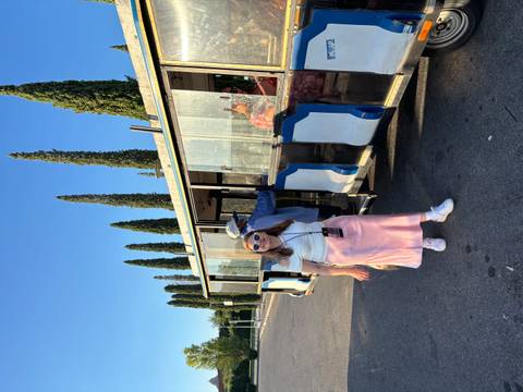 Woman posing near a tourist tram with trees in the background.