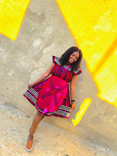 Individual posing against a colorful wall in traditional attire.