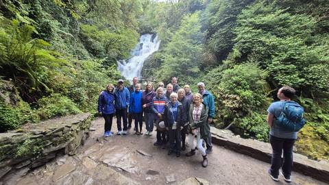       Group of people in front of a waterfall in a lush forest, Ireland.
  
