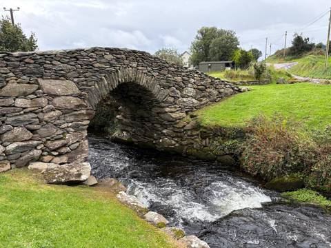 Stone bridge over a flowing river, lush greenery surrounds, Ireland.