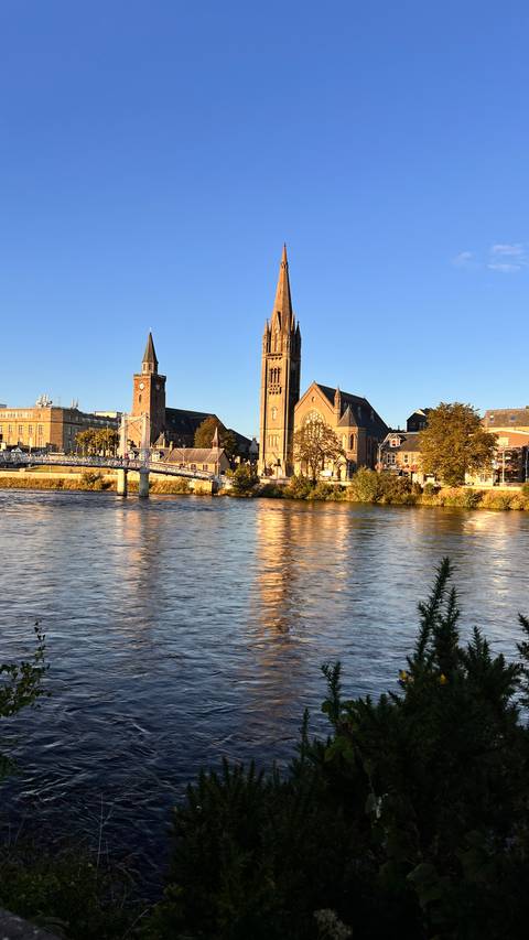 A church and clock tower by a river in golden sunset light.