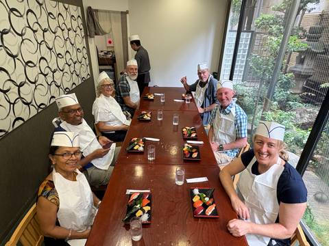       Group of people sitting at a table preparing sushi indoors.
  