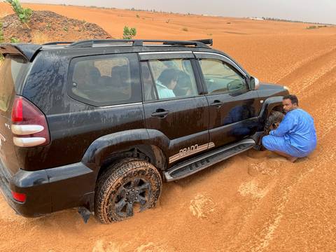 People fixing a vehicle stuck in the desert sand.