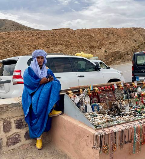       Person in blue attire near a souvenir stall, cars in the background.
  