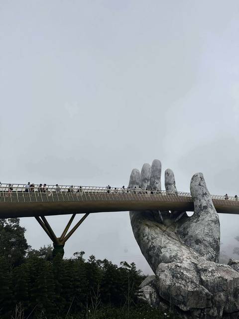 Golden Bridge held by giant stone hands with tourists walking.