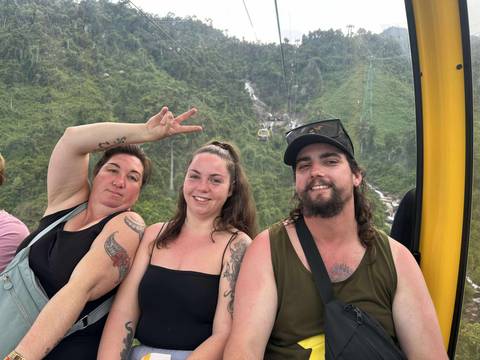 Three people inside a cable car with a view of mountains outside.