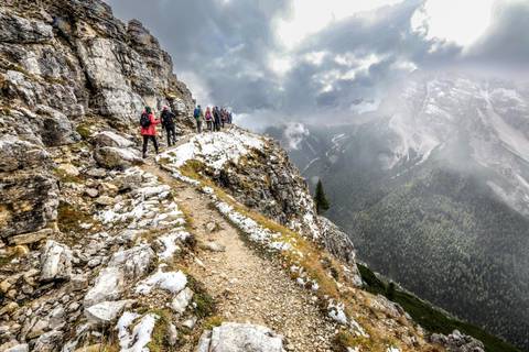 Hikers walking along a narrow mountain path with snow.