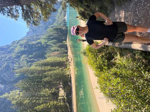       Person by a turquoise lake with forested mountains.
  
