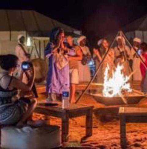 People gathered around a campfire with cultural attire and music.