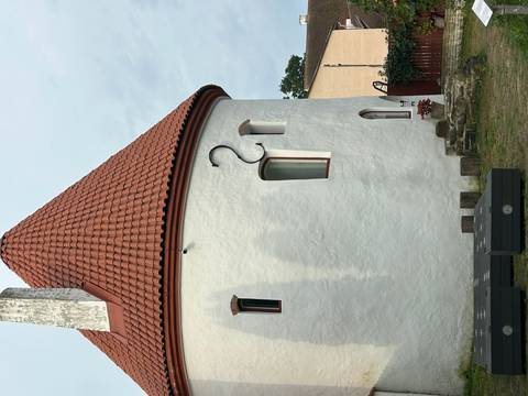       White round building with a red roof against a cloudy sky.
  