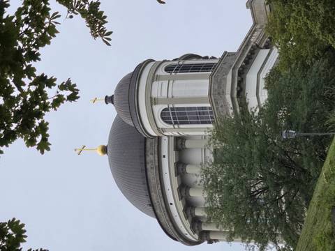       Dome and cross architecture behind trees.
  