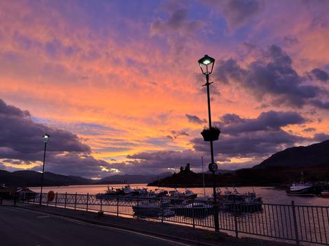       Sunset over a harbor with boats silhouetted against colorful sky.
  