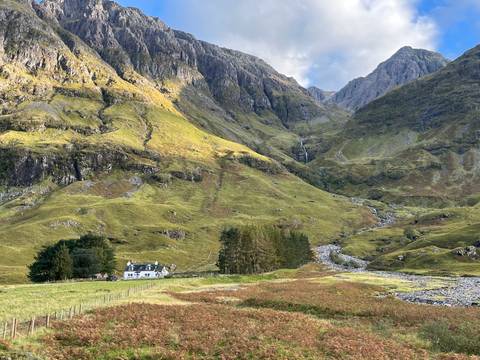       Cottage at the base of large green mountains.
  