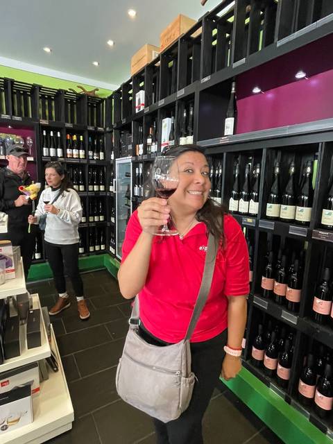 Person raising a wine glass inside a wine shop with others browsing.