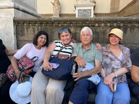 Group of people sitting on a bench smiling, holding bags.