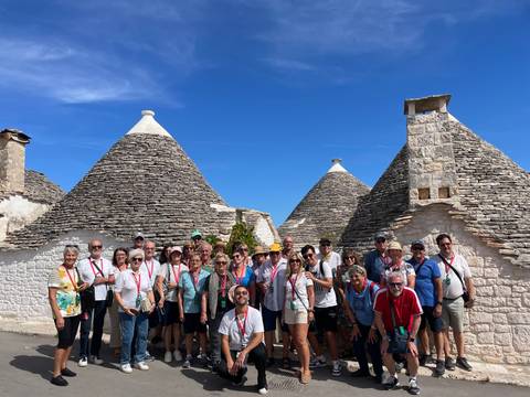 Large group of tourists in front of traditional stone houses with conical roofs.