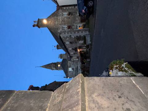      A street view at dusk with stone buildings and a clock tower.
  