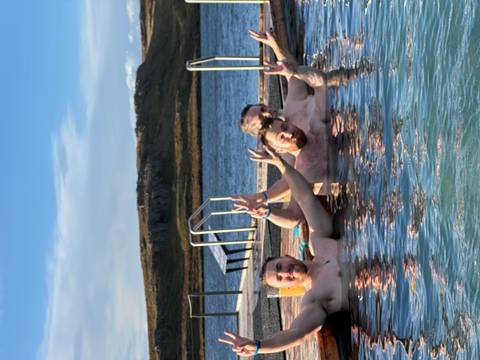 Three people relaxing in a hot spring with outdoor scenery.