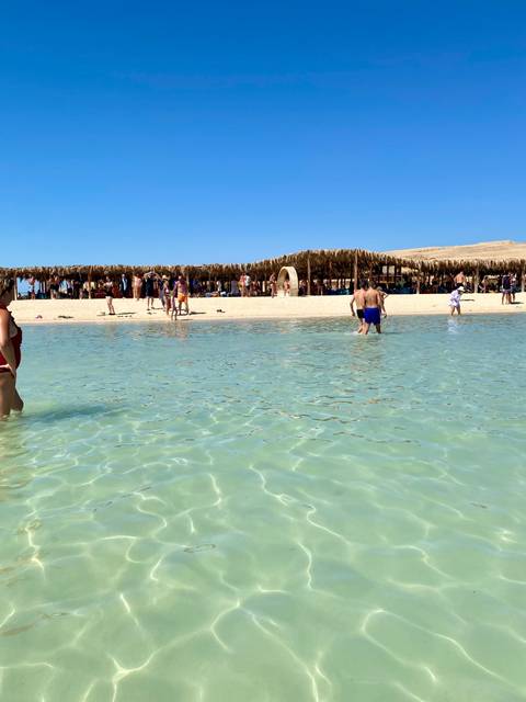       People enjoying a sandy beach with shallow clear water.
  