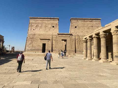       Ancient stone temple with tourists walking towards it.
  