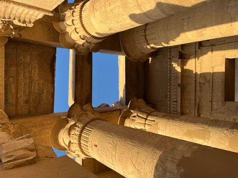       Ancient columns with intricate carvings under a clear sky.
  