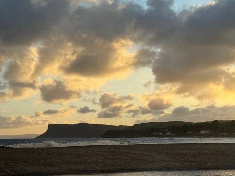 Evening beach view with golden sky and clouds.