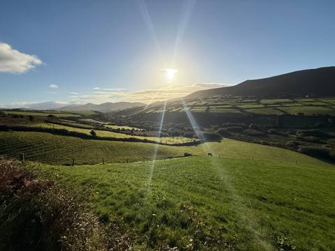 Green countryside with mountains and sun shining.