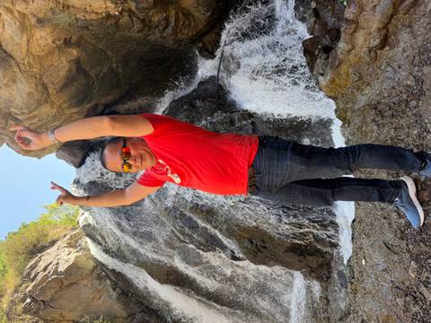       Man posing in front of a waterfall, raising arms in celebration.
  