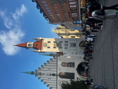 Crowded plaza in front of Munich's New Town Hall with a bright blue sky.
