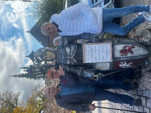       Three men posing with a knight statue outdoors.
  