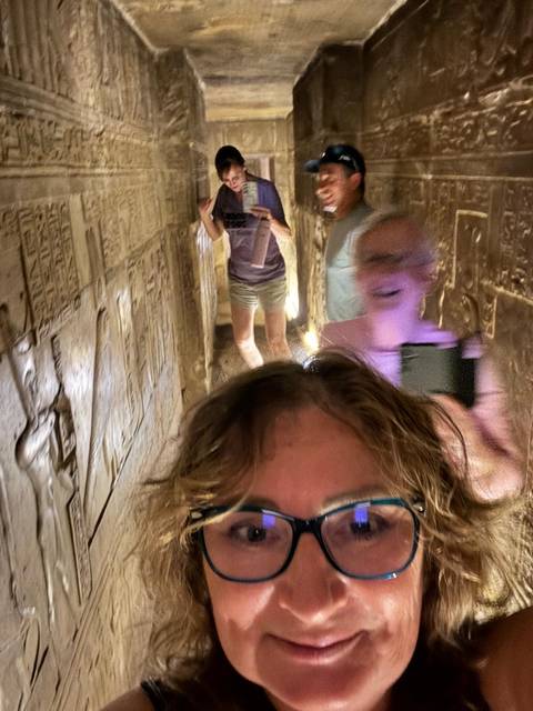 People inside a narrow ancient passageway with hieroglyphs.