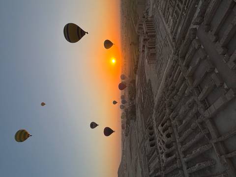 Hot air balloons rising over ancient ruins at sunrise.