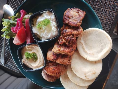 A plate of grilled meat with sauces and flatbread.