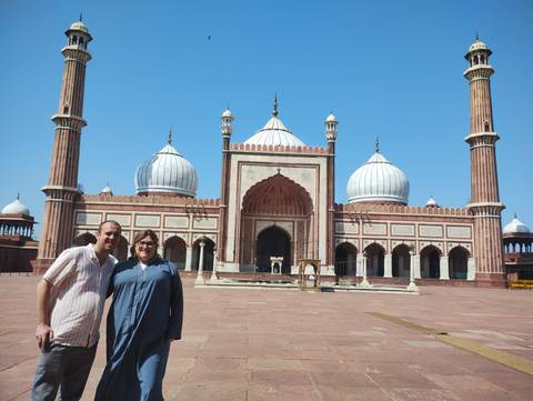 Two people standing in front of a grand mosque with large domes.
