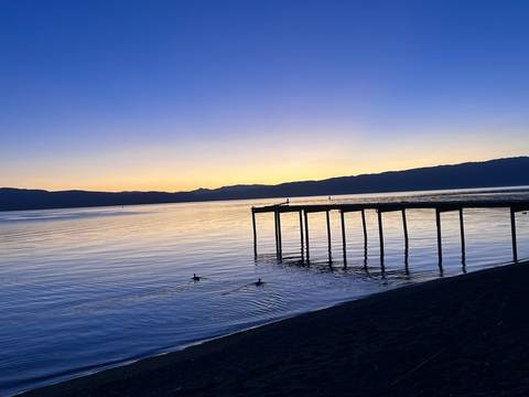 Sunset over a calm lake with a wooden pier and ducks swimming.