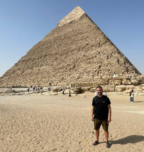 Tourist posing in front of a pyramid with other tourists.
