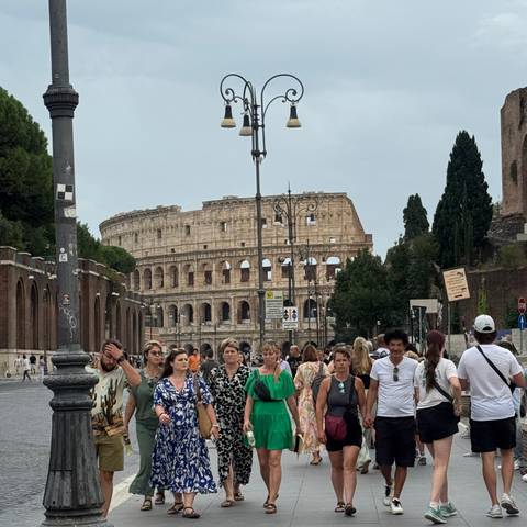       The Colosseum in the background with a crowd of people in the foreground on a cloudy day.
  