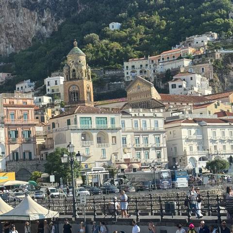       A coastal town with colorful historic buildings and a bell tower against a hillside.
  