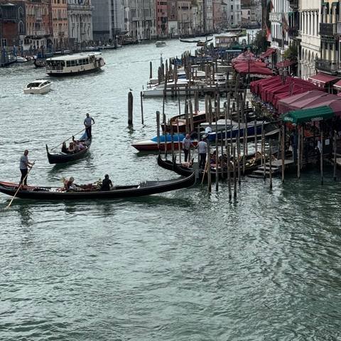       Gondolas on a canal with people disembarking, under an overcast sky.
  