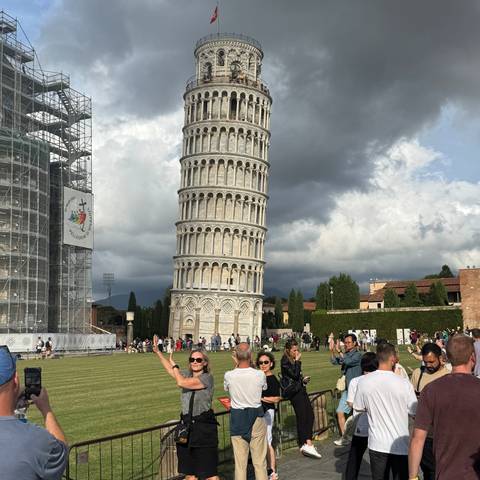       Visitors posing near the Leaning Tower of Pisa on a cloudy day.
  