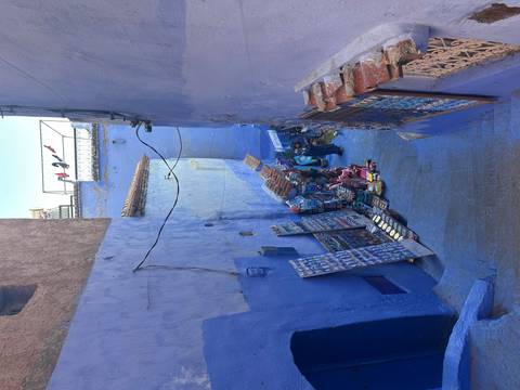 Narrow blue alley with street vendors selling goods.