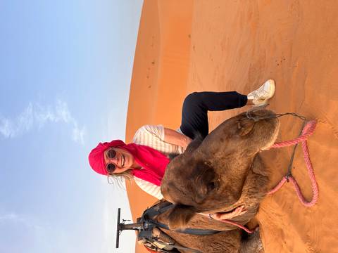 A person wearing red with a camel in the desert.