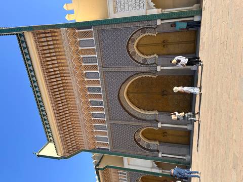 People walking outside an ornately decorated building with arches.