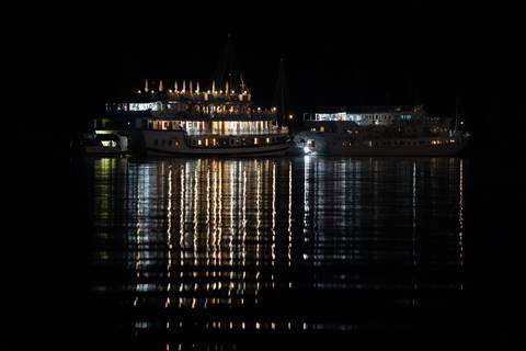       Boats lit up with colorful lights at night, reflecting on water.
  