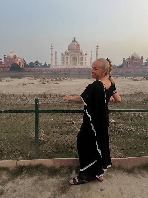       Person in black dress posing with a distant view of Taj Mahal.
  