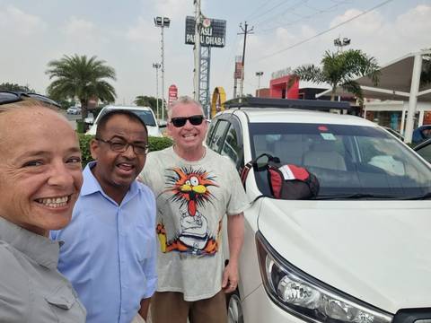       Three people with a car on a sunny day.
  